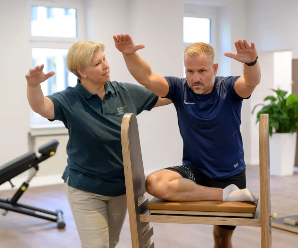 Mann trainiert am Gymwood-Gerät zur Dehnung der Hüfte bei PhysioPunkt Brühl unter Anleitung einer Physiotherapeutin