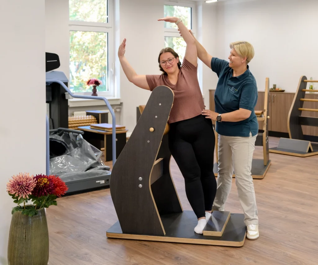 Junge Frau führt Seitbeuge am Gymwood-Gerät bei PhysioPunkt Brühl mit Unterstützung einer Physiotherapeutin aus