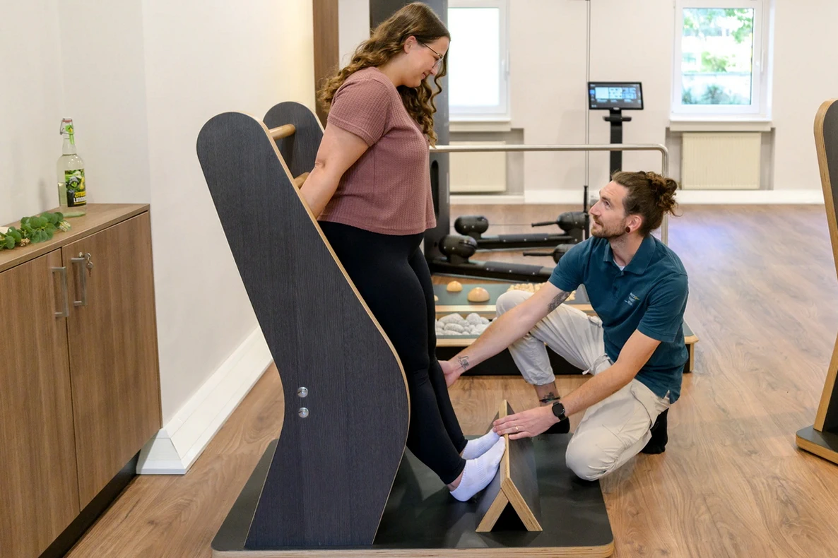 Patientin führt unter Anleitung eines Therapeuten Waden-Dehntraining am Gymwood-Gerät bei PhysioPunkt Brühl durch