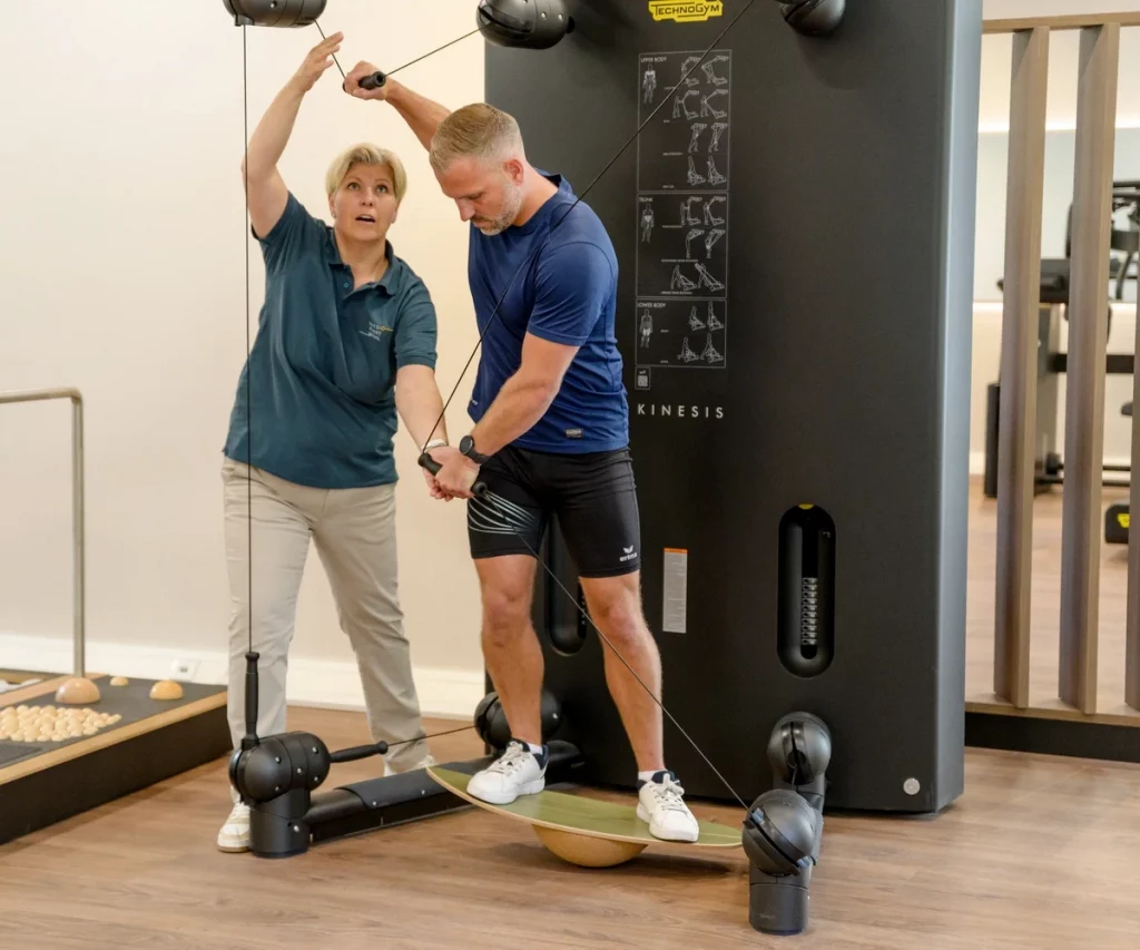 Patient trainiert an der Kinesis One mit instabiler Unterlage bei PhysioPunkt Brühl, unterstützt durch Physiotherapeutin