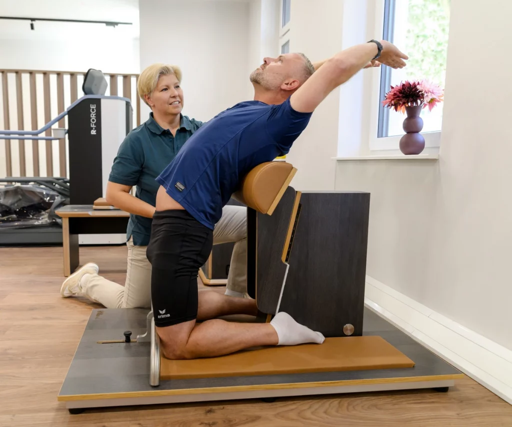 Mann trainiert am Gymwood-Gerät zur Verbesserung der Beweglichkeit bei PhysioPunkt Brühl unter Anleitung einer Physiotherapeutin