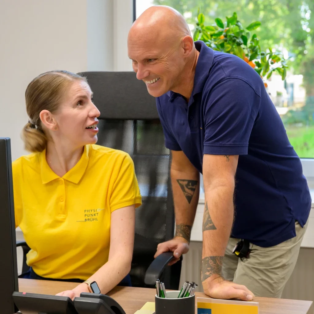 Mitarbeitende von Physiopunkt Brühl im Gespräch am Empfang – Teamarbeit und Kommunikation im Praxisalltag