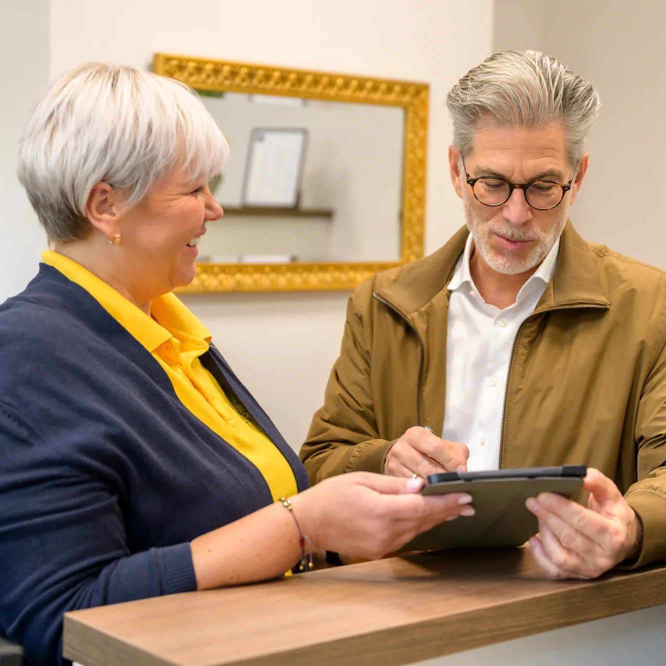 Mitarbeiterin von Physiopunkt Brühl berät einen Patienten freundlich am Front Desk mit Tablet
