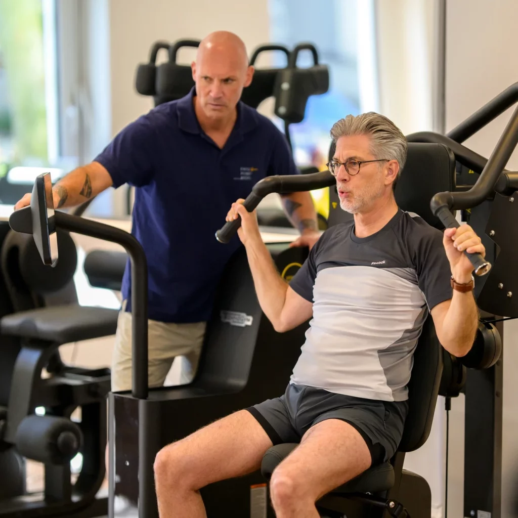 Patient führt unter Anleitung eines Therapeuten gezieltes Krafttraining an Geräten im Rahmen der T-RENA bei PhysioPunkt Brühl durch.