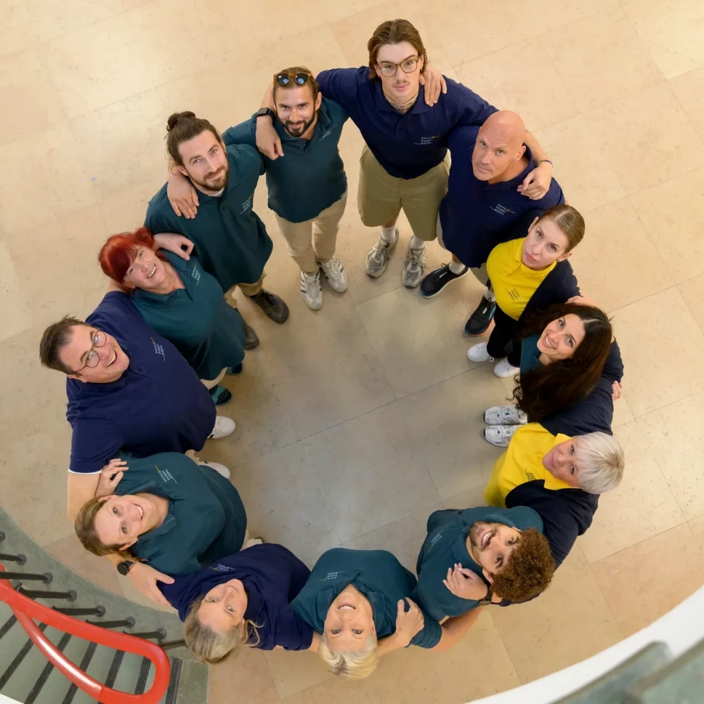 Das Team von Physiopunkt Brühl steht im Kreis zusammen und blickt lächelnd nach oben – Symbol für Zusammenhalt und Gemeinschaft.