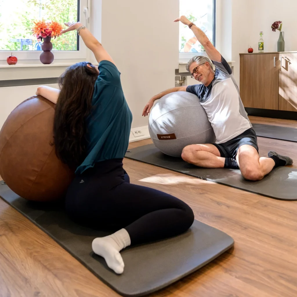 Zwei Teilnehmer beim dynamischen Dehnen mit großen Gymnastikbällen im Präventionskurs Mein Beweglichkeitstraining bei AktivPunkt Brühl.