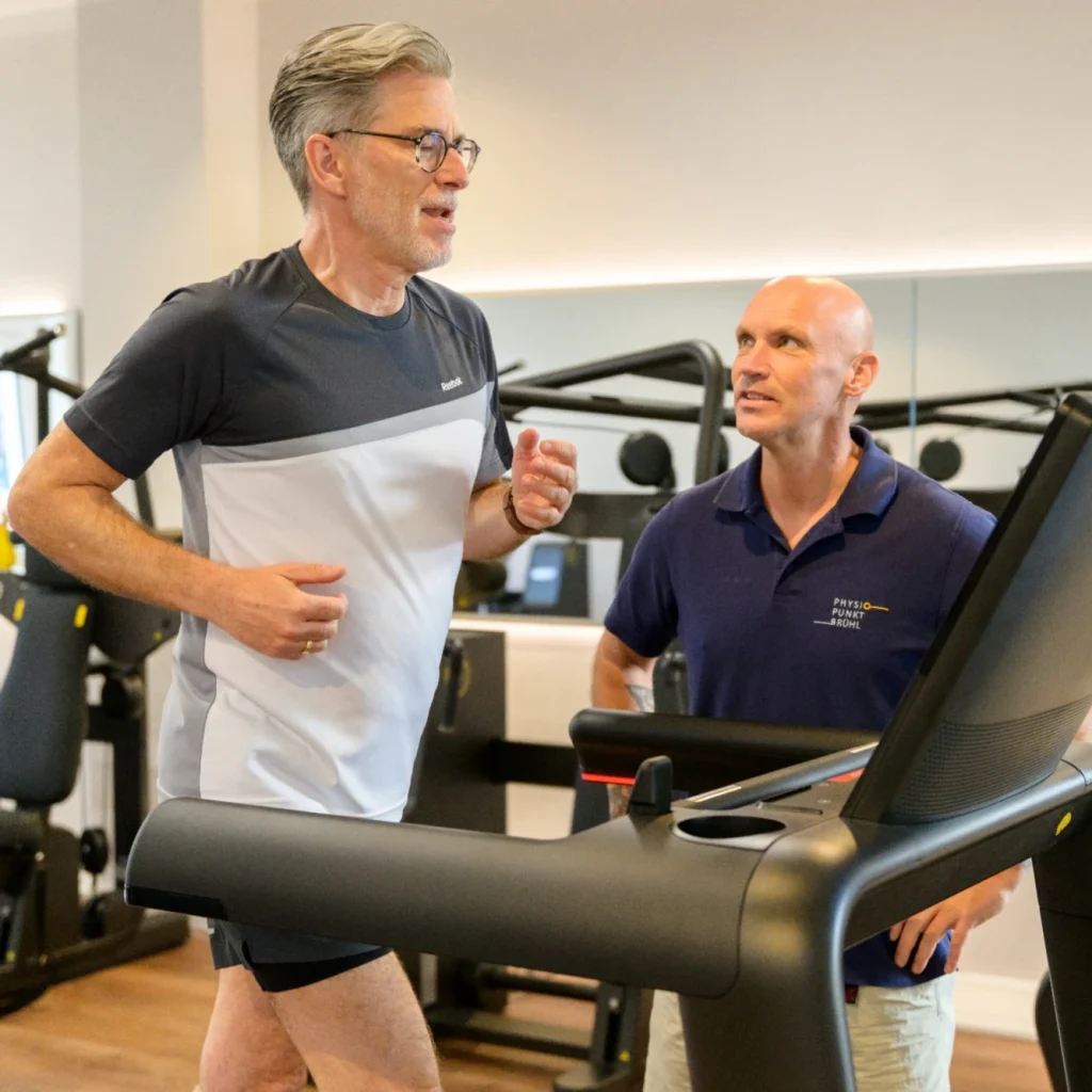 Mann läuft auf einem Laufband, während ein Trainer von PhysioPunkt Brühl ihn direkt begleitet.